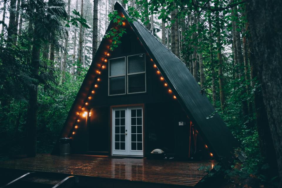 a-frame cabin house with deck and string lights surrounded by tall trees