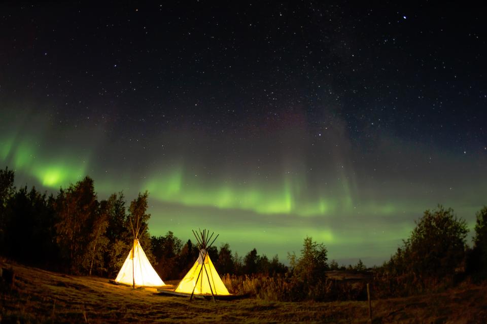 teepee tents at night light up with the northern lights in the background