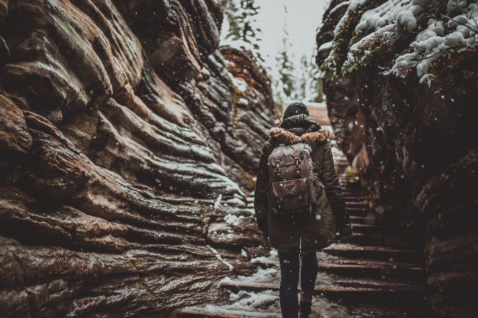 brown cave walls surround a backpacking explorer as snow falls