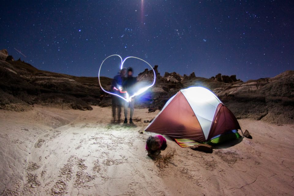 two people light-write a heart while tent camping in the desert under the starry night sky