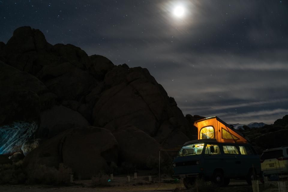 vw bus lights up during the nighttime while parked near tall rocky terrain