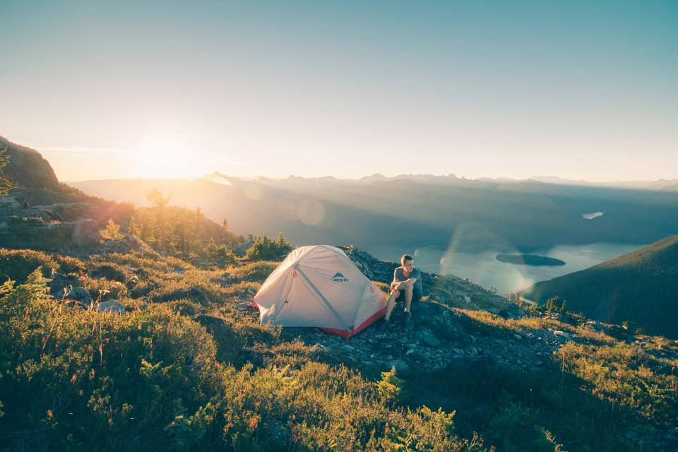 a person sits outside of a white and red tent on a hillside during sunrise