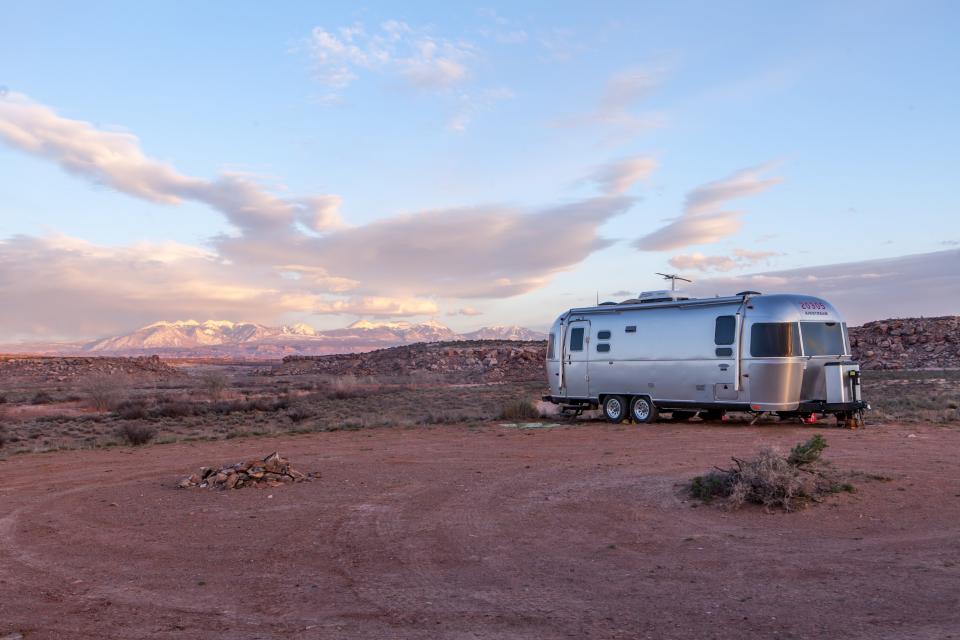 silver airstream camper parked in the desert with a blue sky and clouds above