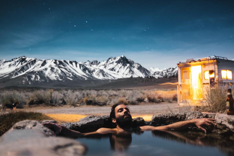 a man lounges in a hot spring with a snow-capped mountain in the distance