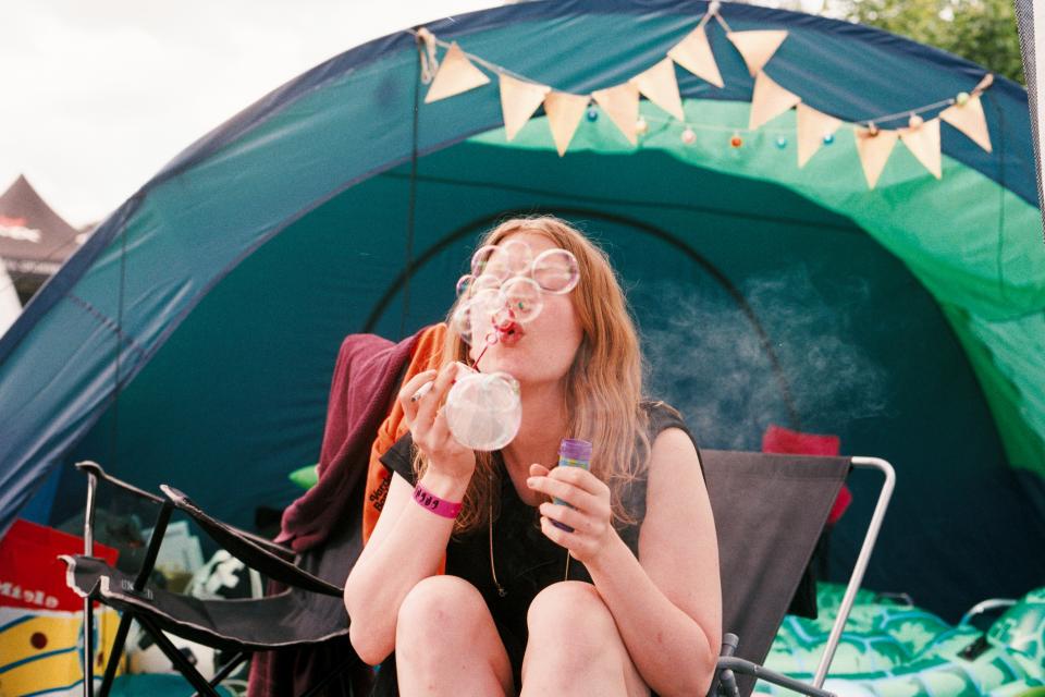 woman with red hair blowing bubbles while sitting in a lawn chair outside of a green tent
