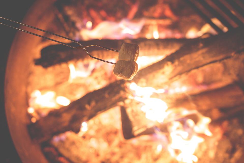 two marshmallows on a skewer roast above a campfire flame