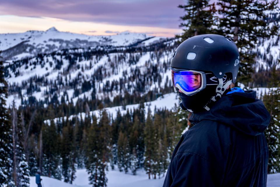 person wearing ski goggles and helmet with mountains and trees in the distance