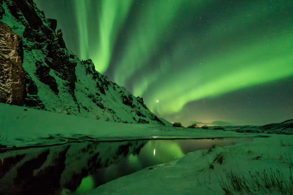 snowy mountain range near body of water with auroras in the sky above