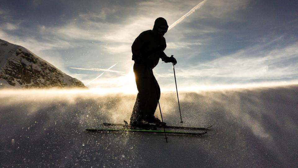 silhouetted figure stands on skiis and descends down a snowy slope