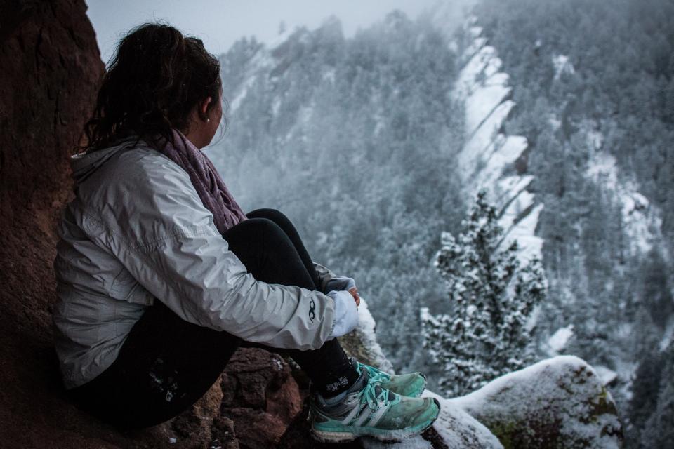 woman sitting on mountainside looking out at a snowy forest