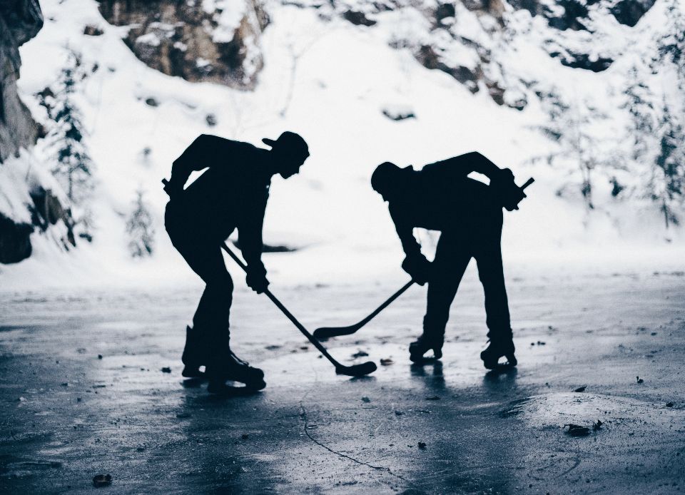 silhouettes of people holding hockey sticks with a snowy hill in the background