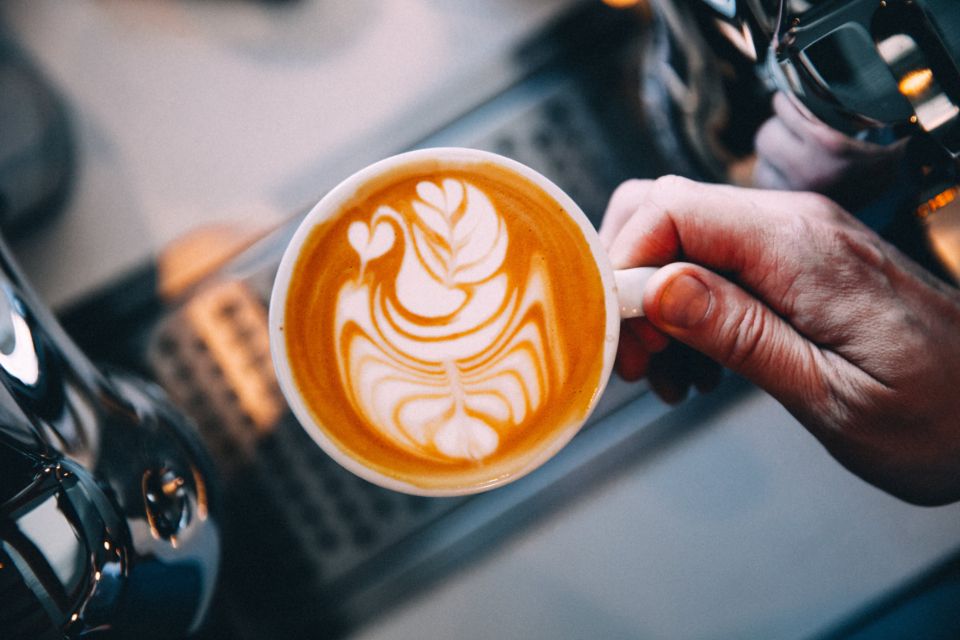 a hand holds an artistic latte in white mug