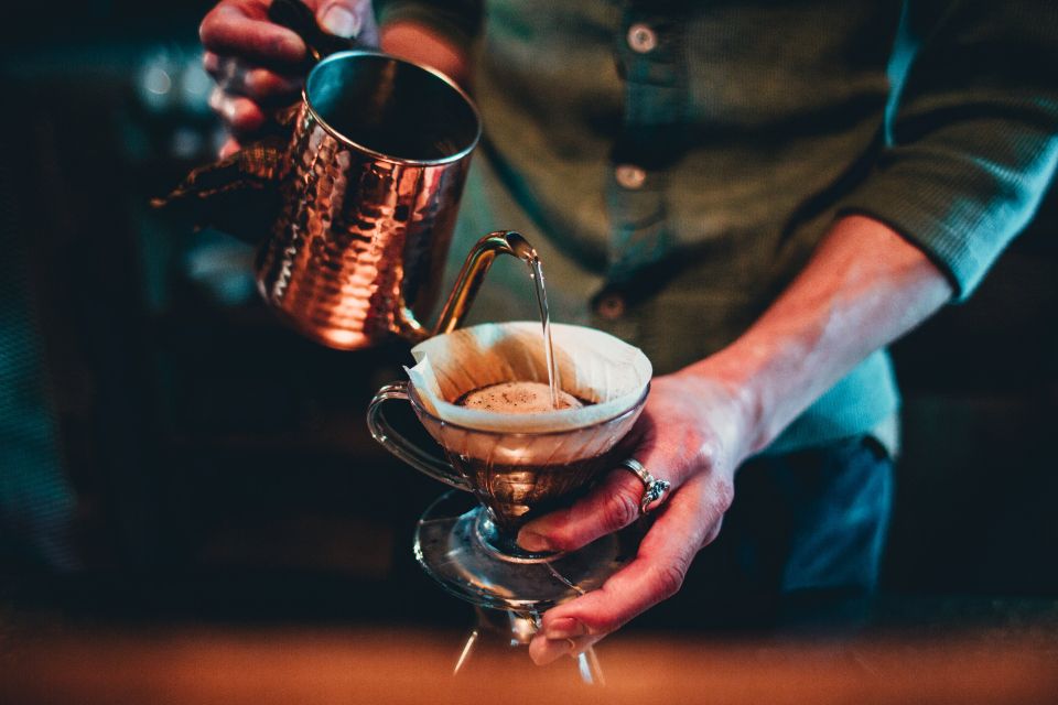 barista wearing a button down shirt pours hot water into a coffee funnel to make a pour-over