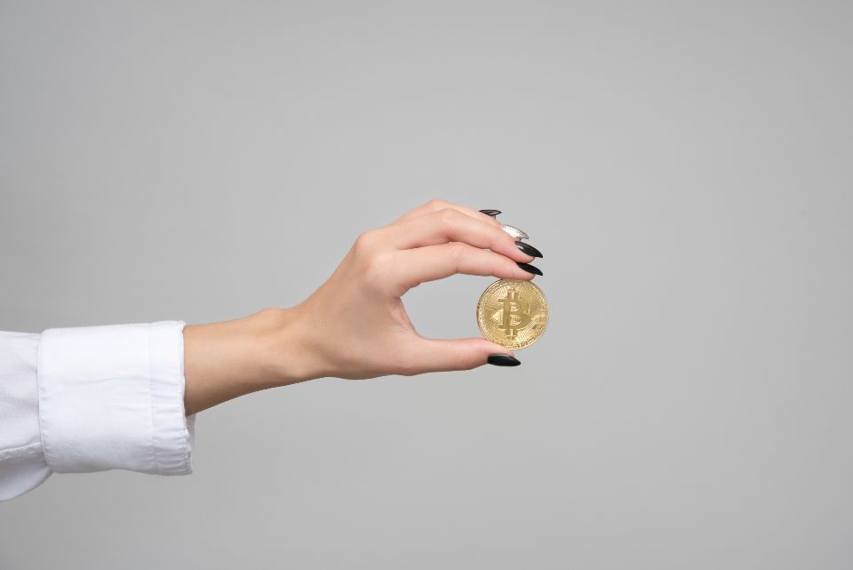 A hand, with black fingernails, holds a physical bitcoin to represent cryptocurrency