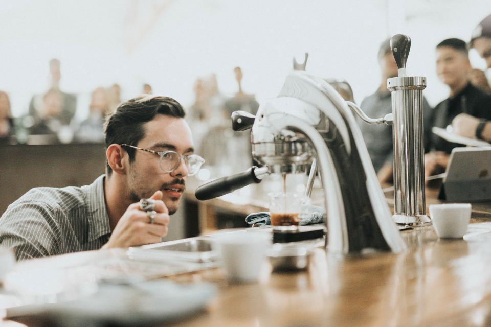 a barista wearing glasses waits for coffee in a crowded cafe