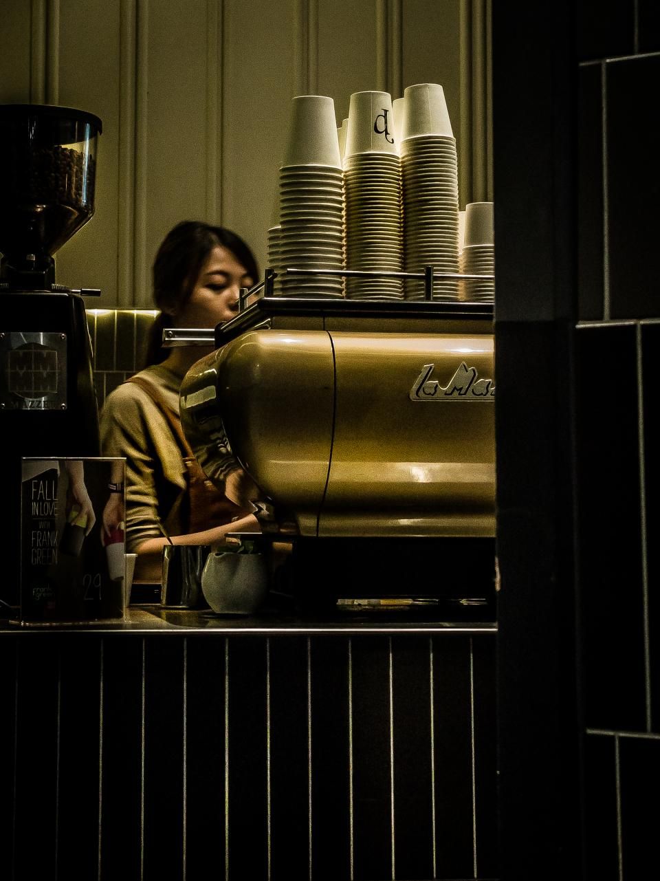woman stands at coffee machine behind a counter at a coffeehouse