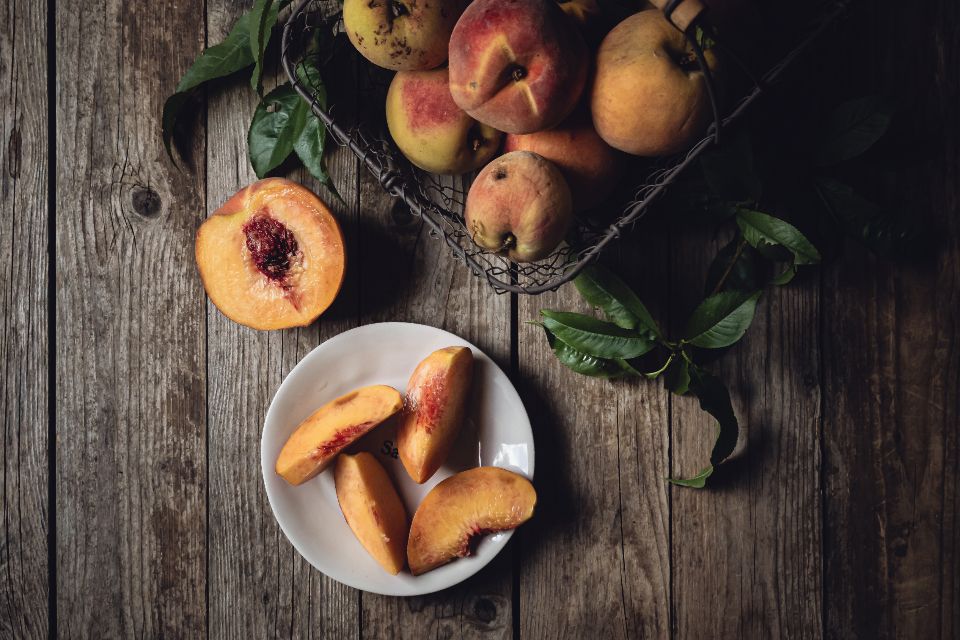 whole and halved peaches sit on a dark rustic, wooden surface