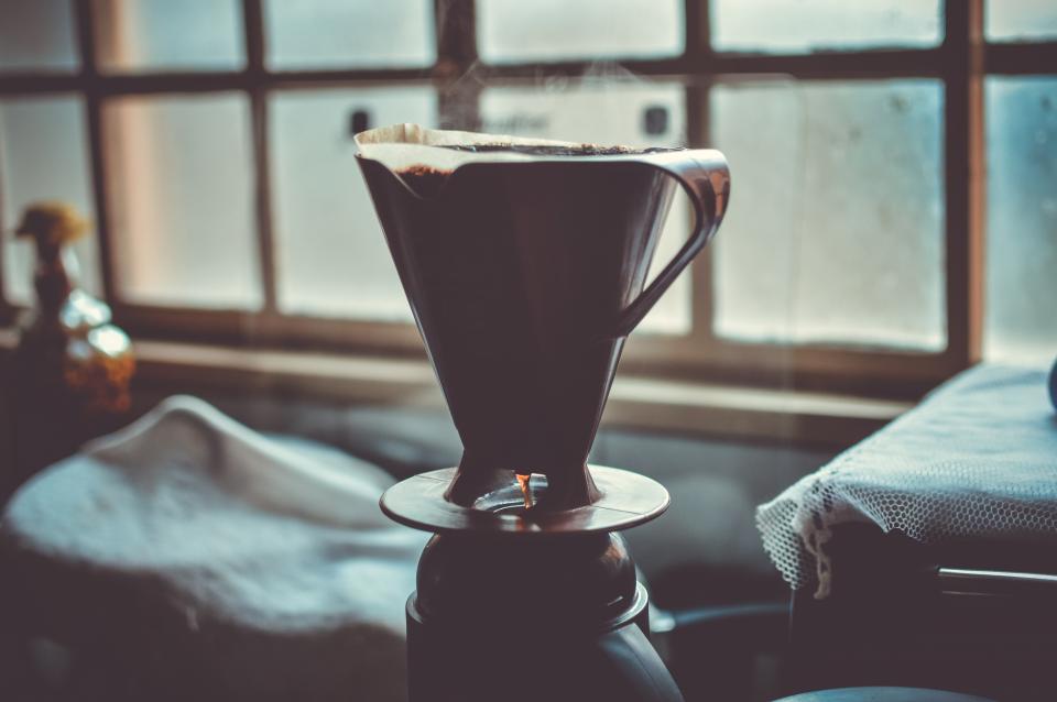 silhouette of a mug with coffee pour-over funnel siting by a window sill