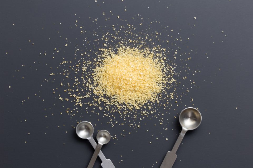 a mound of sugar lies in the center of a gray surface accompanied by three measuring spoons