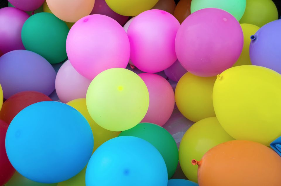 Multiple birthday balloons in an assortment of colors fill the frame of a photograph.