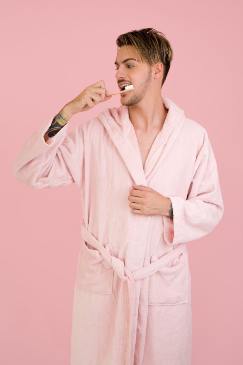Man stands in a pink bathroom against a pink background and brushes his teeth