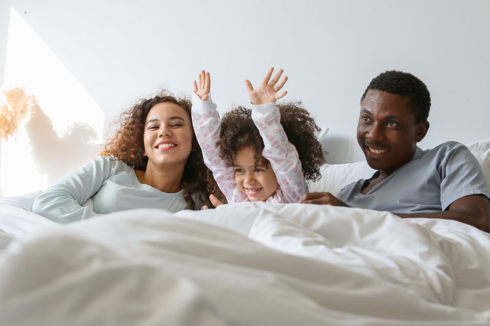 Interracial family of three wake up in a white room, on bed with white linens