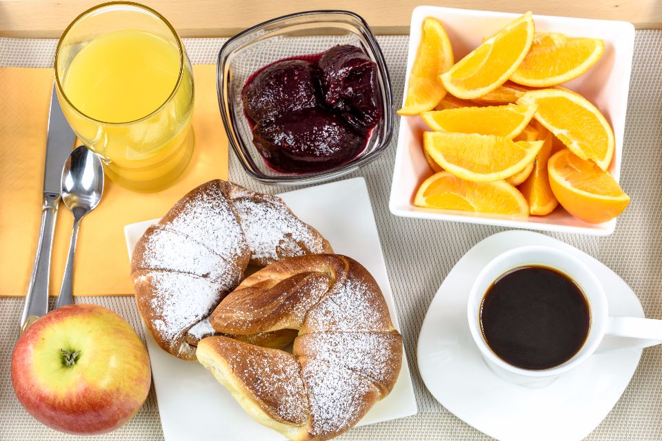 Breakfast consisting of croissants, orange slices, coffee, orange juice and jam