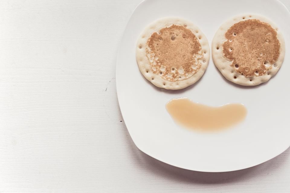 Two pancakes sit on a white plate with syrup, resembling a smiley face.