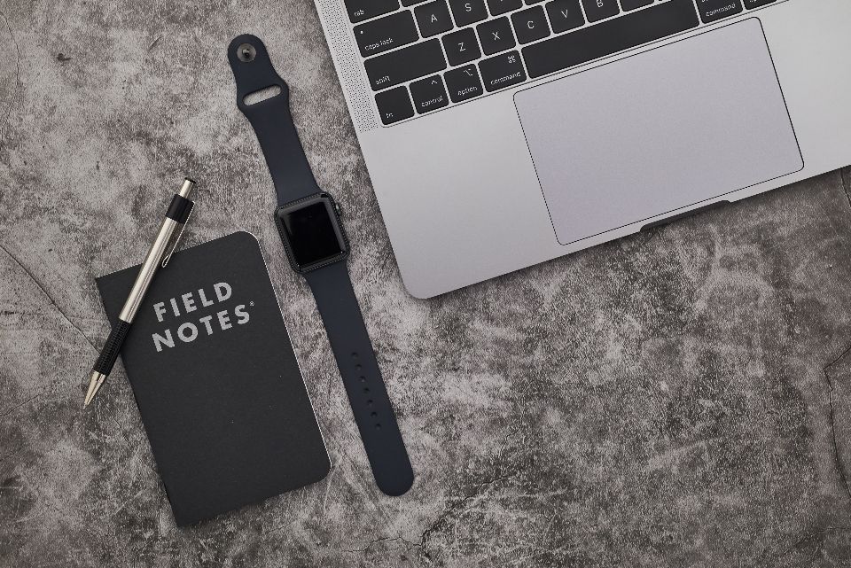 a top-down view of a gray surface with a laptop, watch, notebook and pen