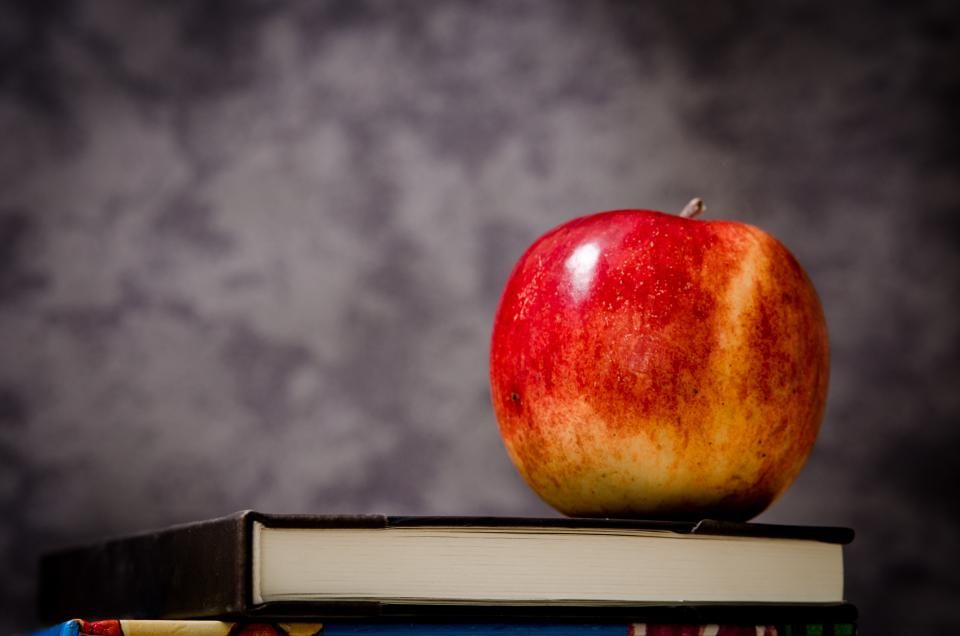 a shiny red apple sits on top of a stack of books