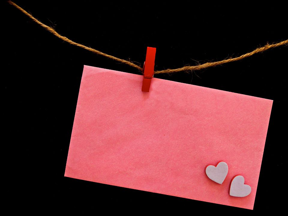 a pink envelope with white hearts hangs from twine