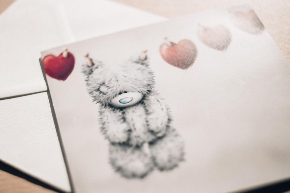 a white envelope and postcard with a bear and red hearts 