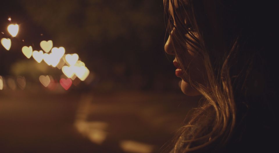 a side profile of a woman standing outside at night time with heart-shaped bokeh lights in the distance