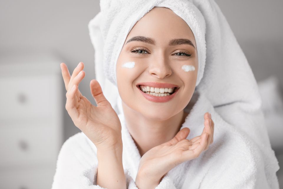 a woman in a white robe has a white towel on her head and skin cream on her face