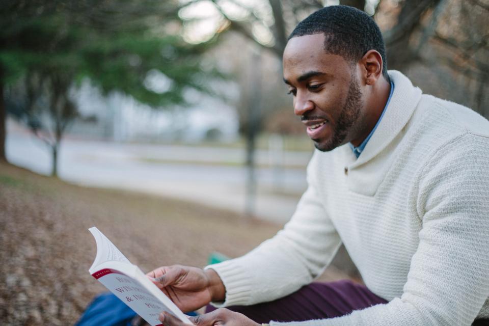a man sits outside and smiles as he reads a book