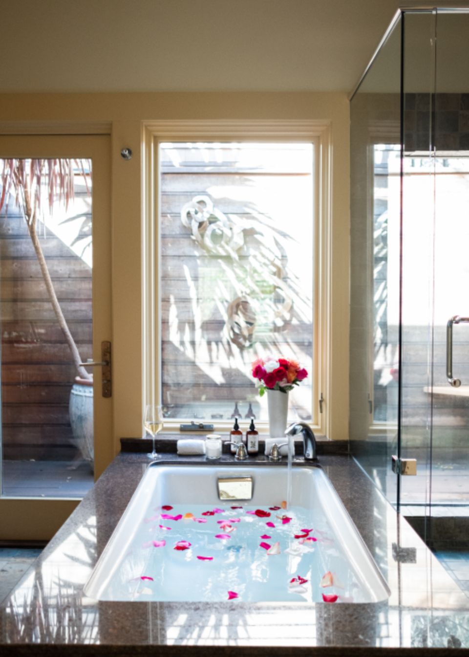 running water in a bath tub with flower petals and a sun lit view