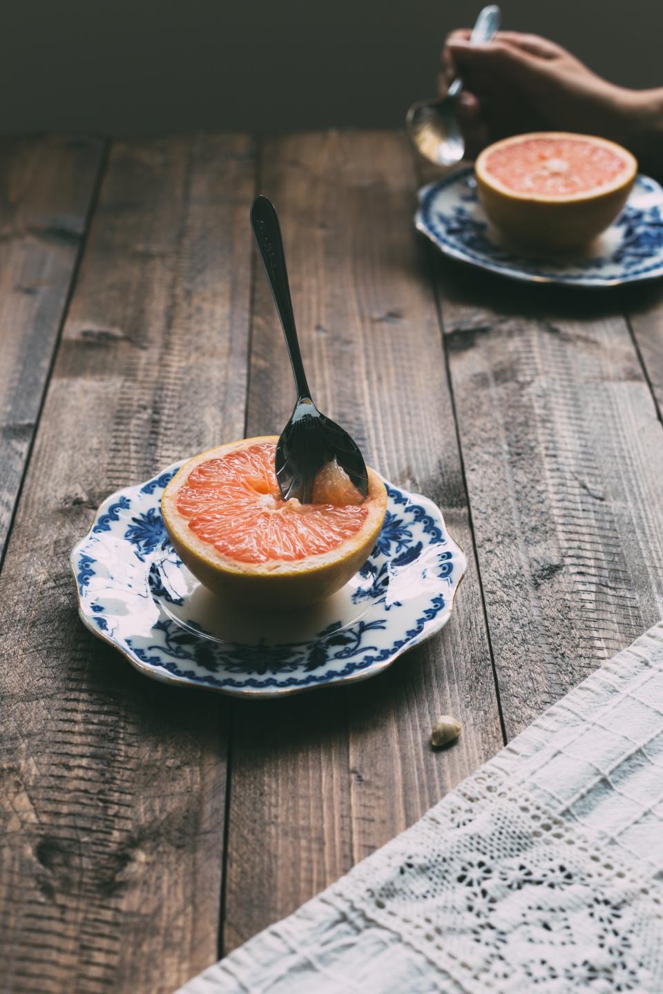 two people eat grapefruits with a spoon, on blue and white porcelain plates