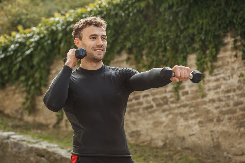 Young man holding two black dumbbells and exercising outdoors. 