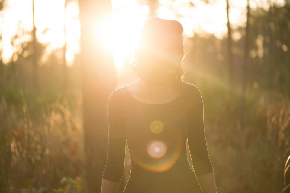 Girl stands in the middle of a forest, saturated by sunlight, during sunrise