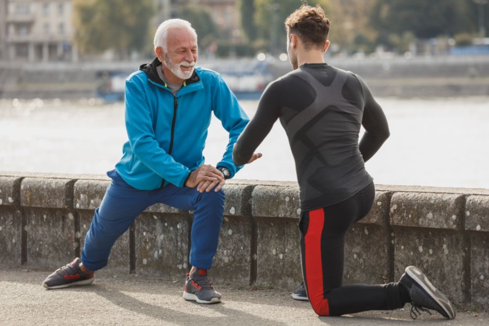 A senior and a young man face each while doing lunges to stretch.