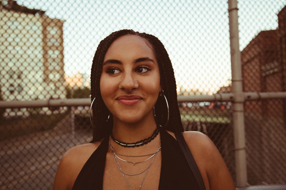 a young woman in a black halter top and silver hoop earrings smirks
