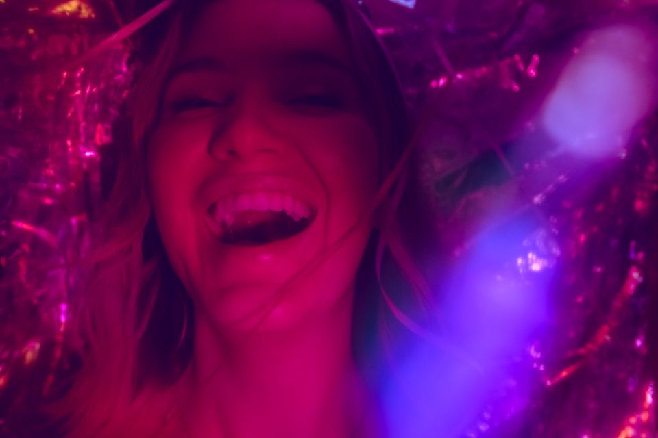 a woman in a nightclub with colorful red, pink and purple-toned lights smiles brightly