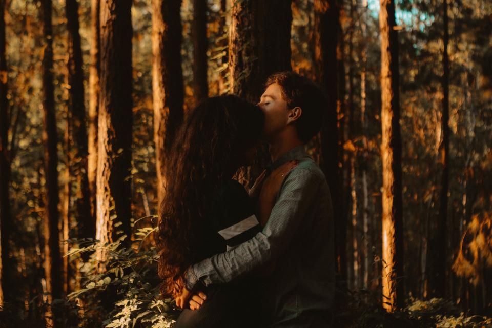 a young couple leans in for an embrace while standing in the forest surrounded by trees