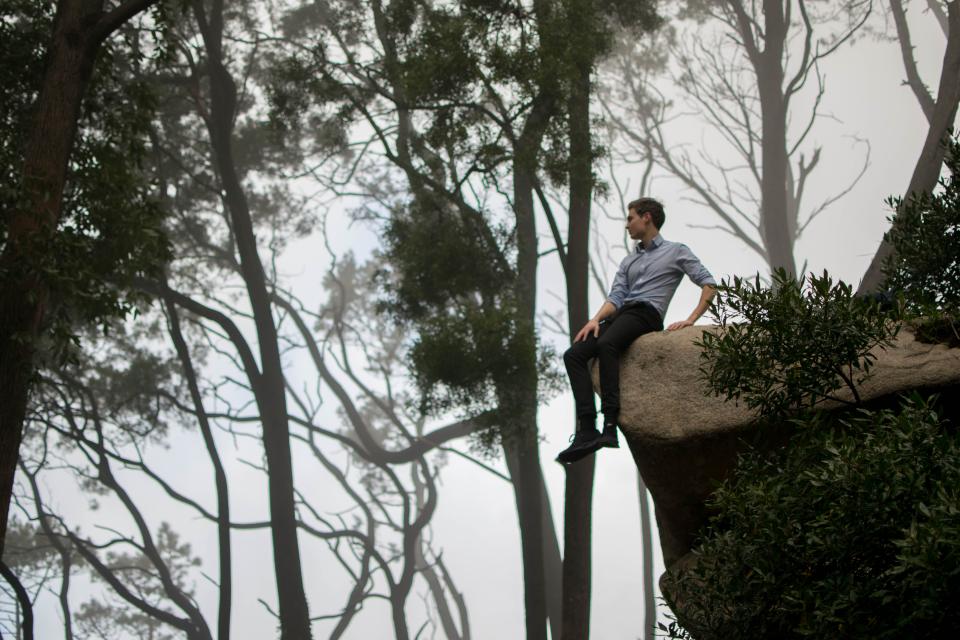 a man sits in nature on the edge of a large rock