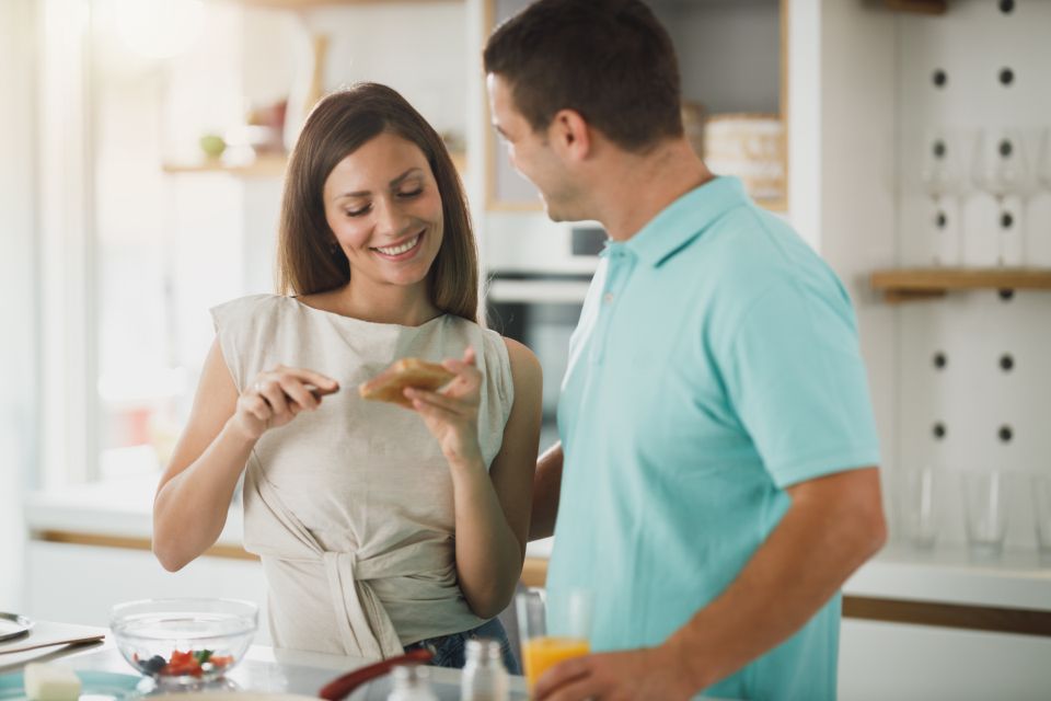 a happy couple prepares breakfast together and smiles at each other.
