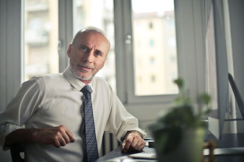 older businessman sitting at desk while wearing a suit and tie