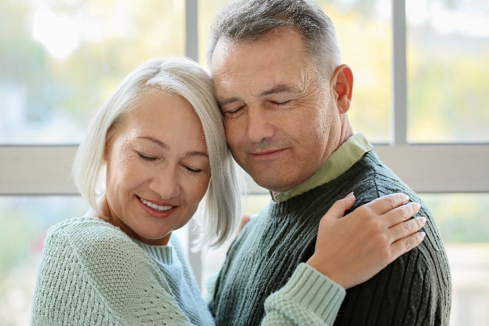 senior couple in green sweaters hugging and smiling sweetly 